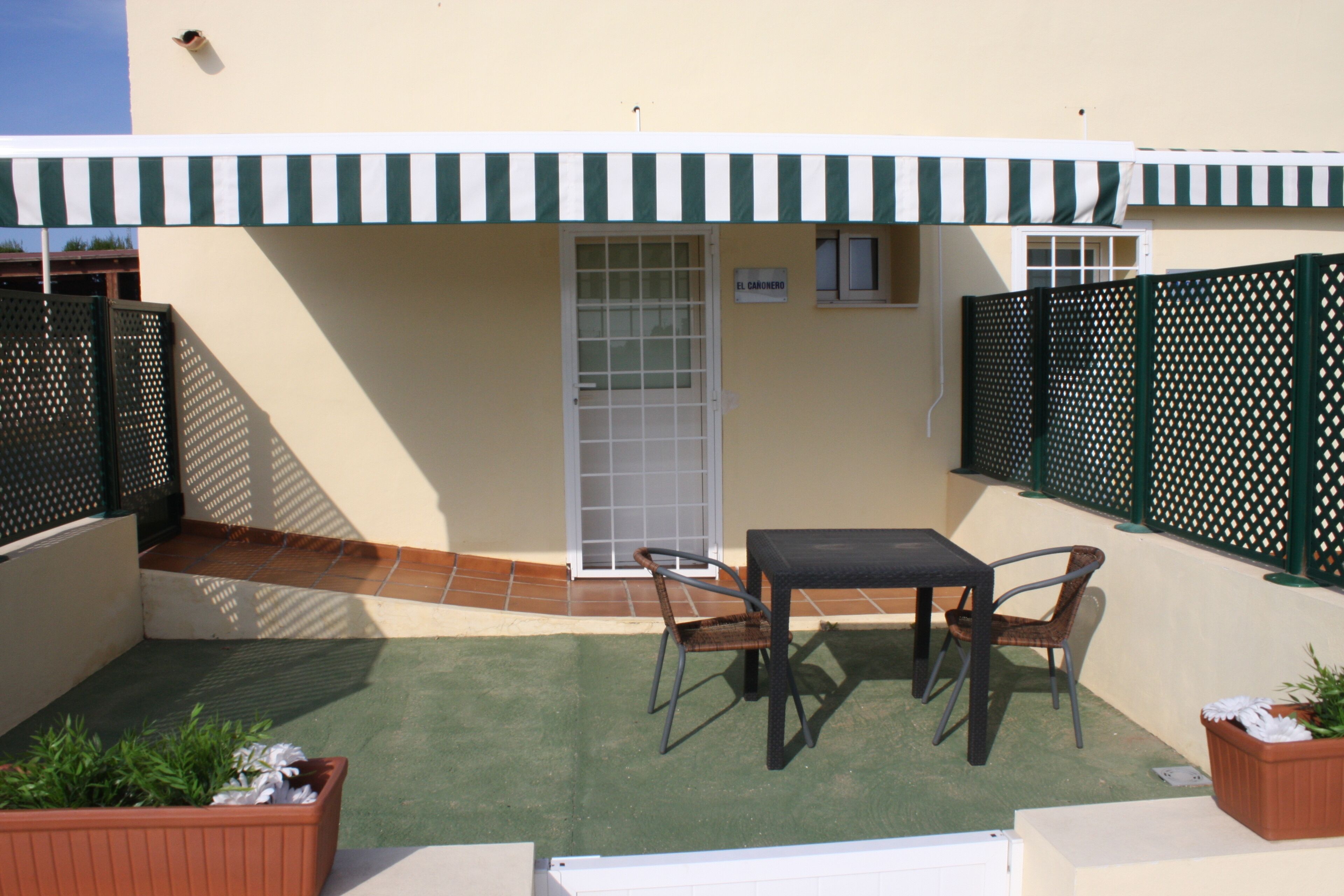 A patio with a table and chairs, a covered area with a striped awning, and a sign reading "EL CARROÑO".