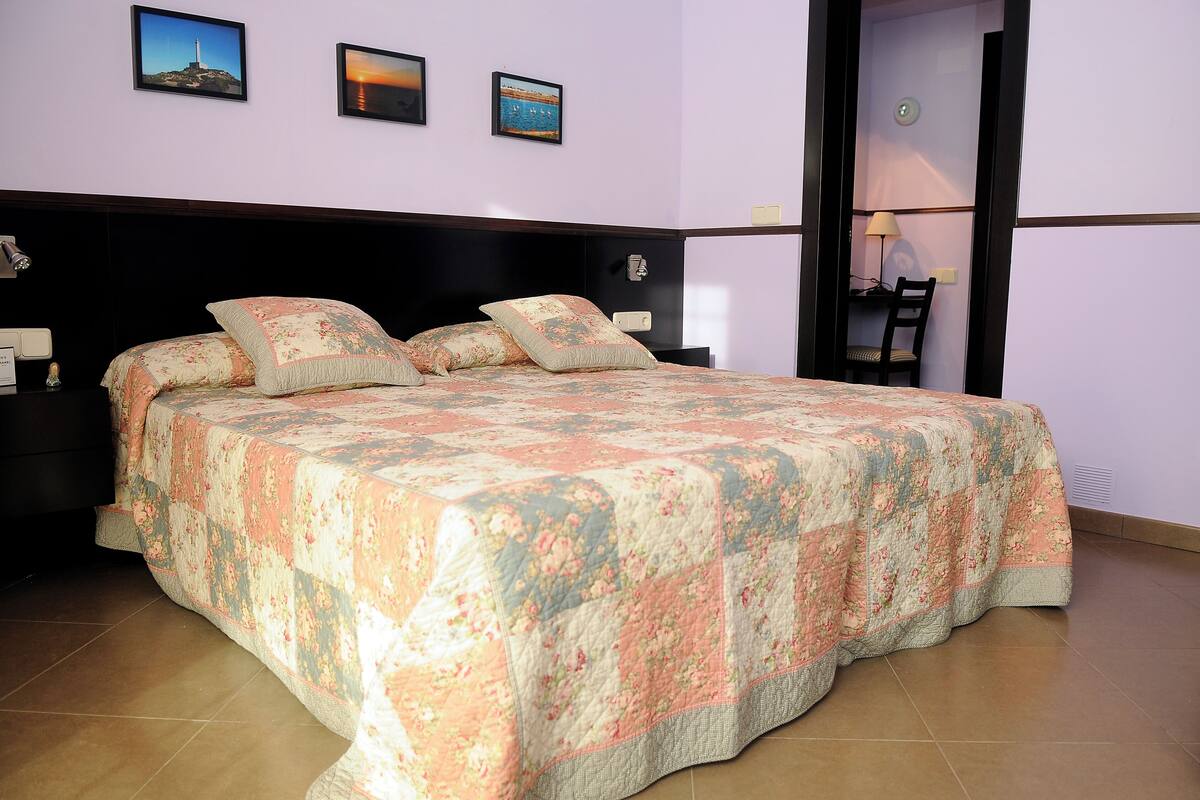 Una cama bien tendida con ropa de cama floral, un cabecero de madera y una mesita de noche con una lámpara.