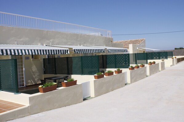 A modern building with a flat roof, a covered outdoor seating area, and potted plants along the exterior walls.