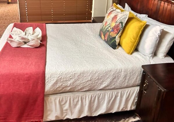 Una cama bien hecha con colcha blanca, una manta roja y almohadones decorativos.
