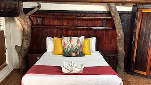 Una cama con una colcha roja, almohadas blancas y un cojín estampado con flores.