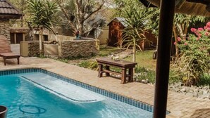 Una piscina con borde de piedra, rodeada por un patio con mesa y sillas.