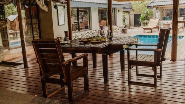 Una terraza de madera con una mesa de billar, sillas y una piscina.