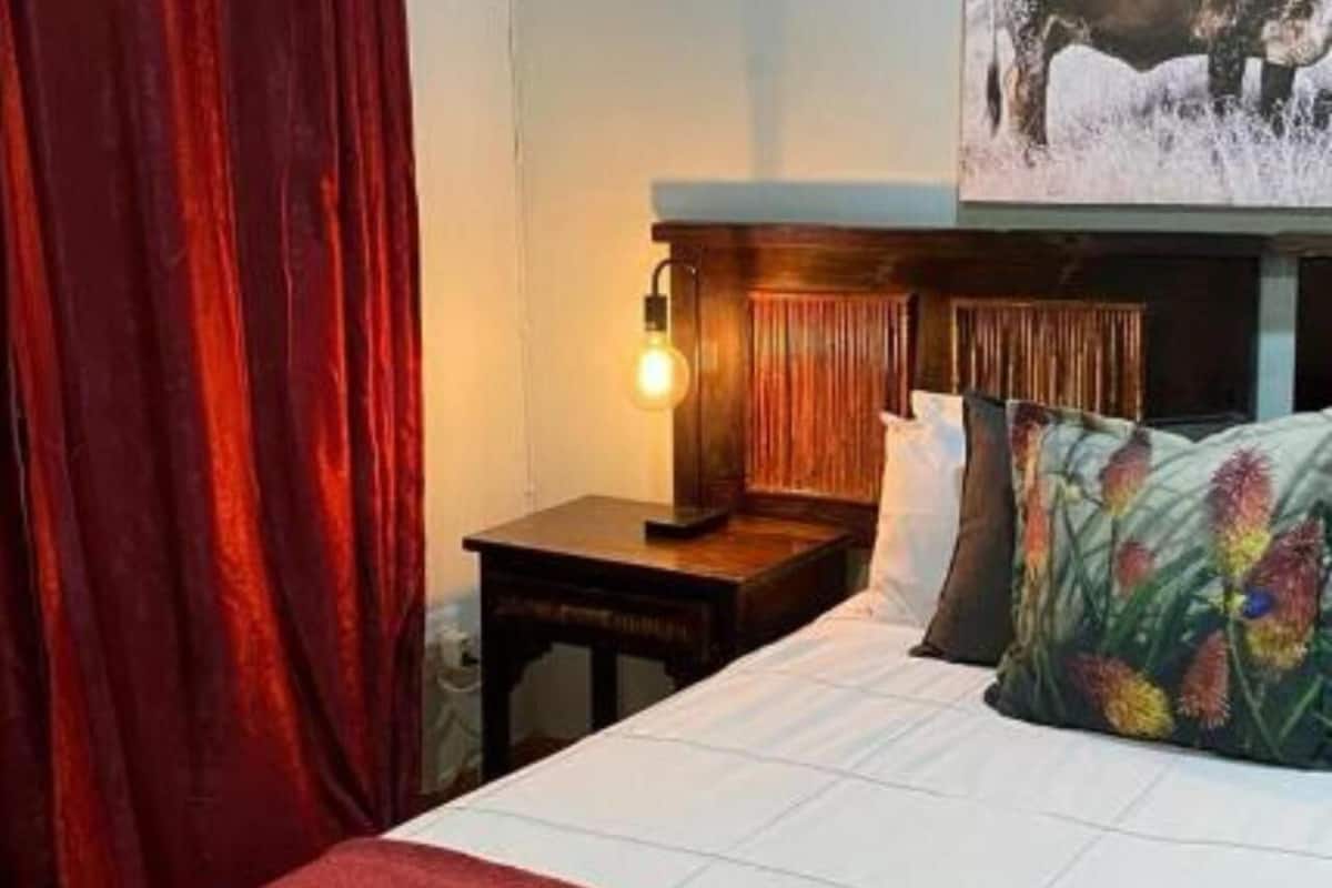 A hotel room with a bed, a nightstand, a lamp, and a painting on the wall.