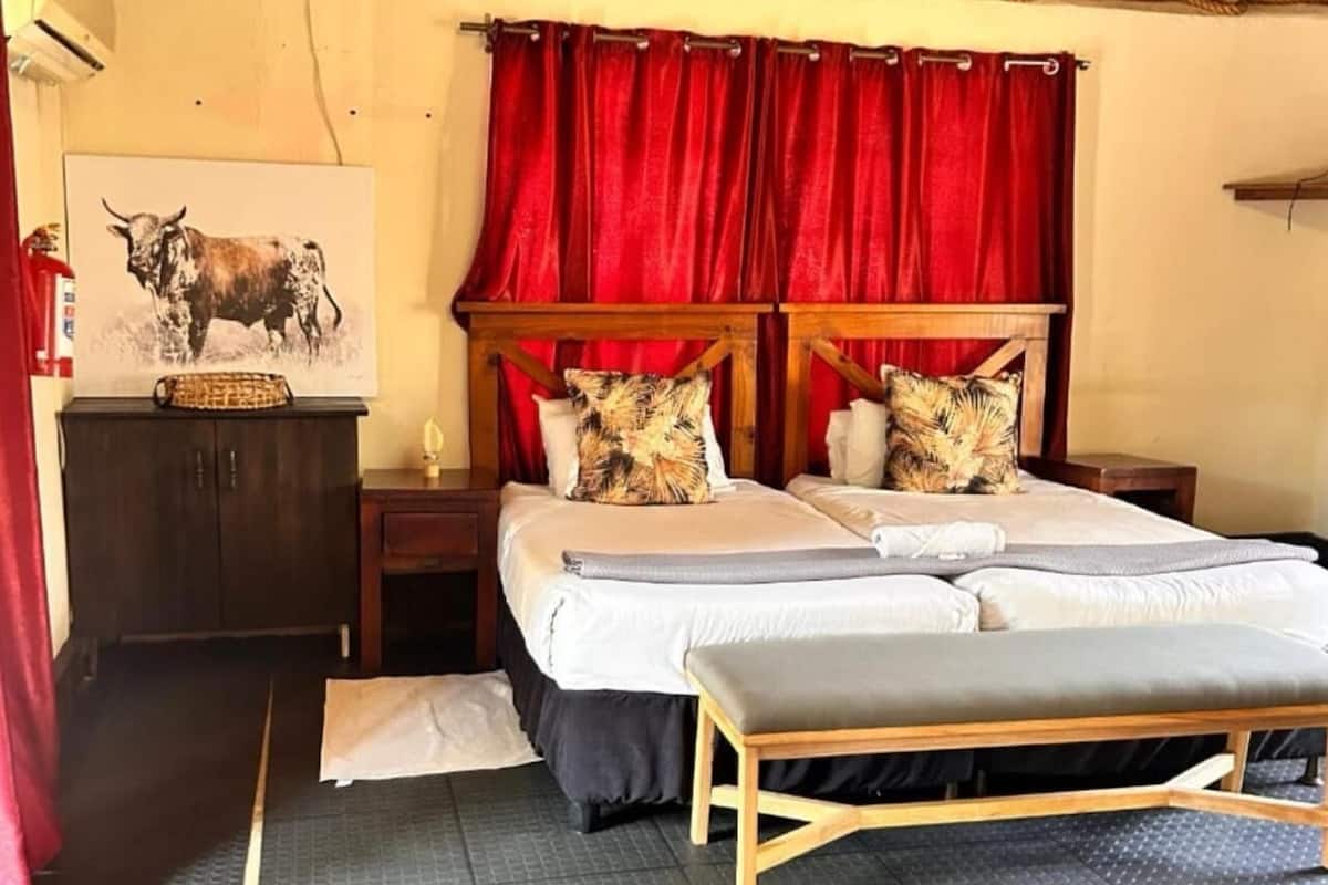 A bedroom with a large bed, two nightstands, a wooden bench, a red curtain, and a bull painting on the wall.