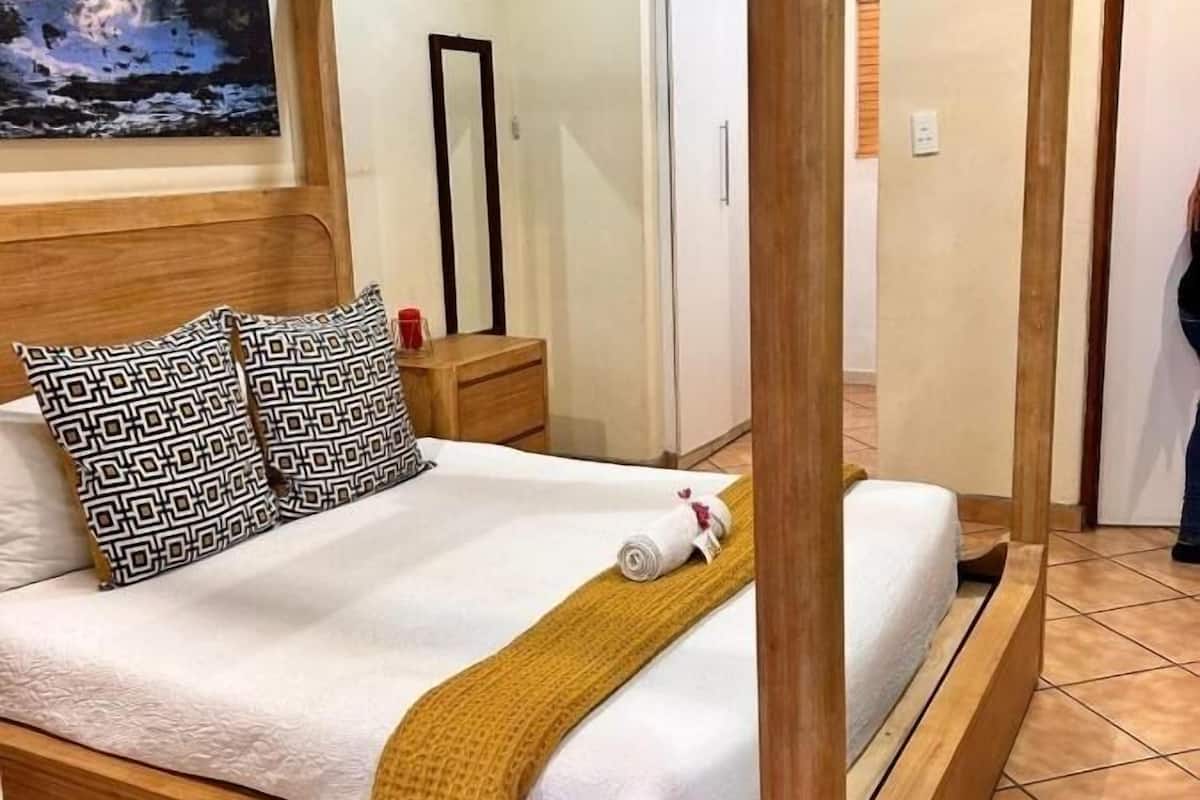A four-poster bed with a wooden frame, a white bedspread, patterned pillows, and a rolled towel.