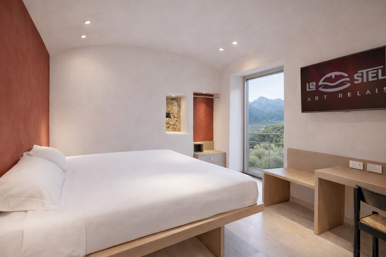 Habitación de hotel moderna con una cama grande, un escritorio, una silla, un televisor y vista a la montaña.