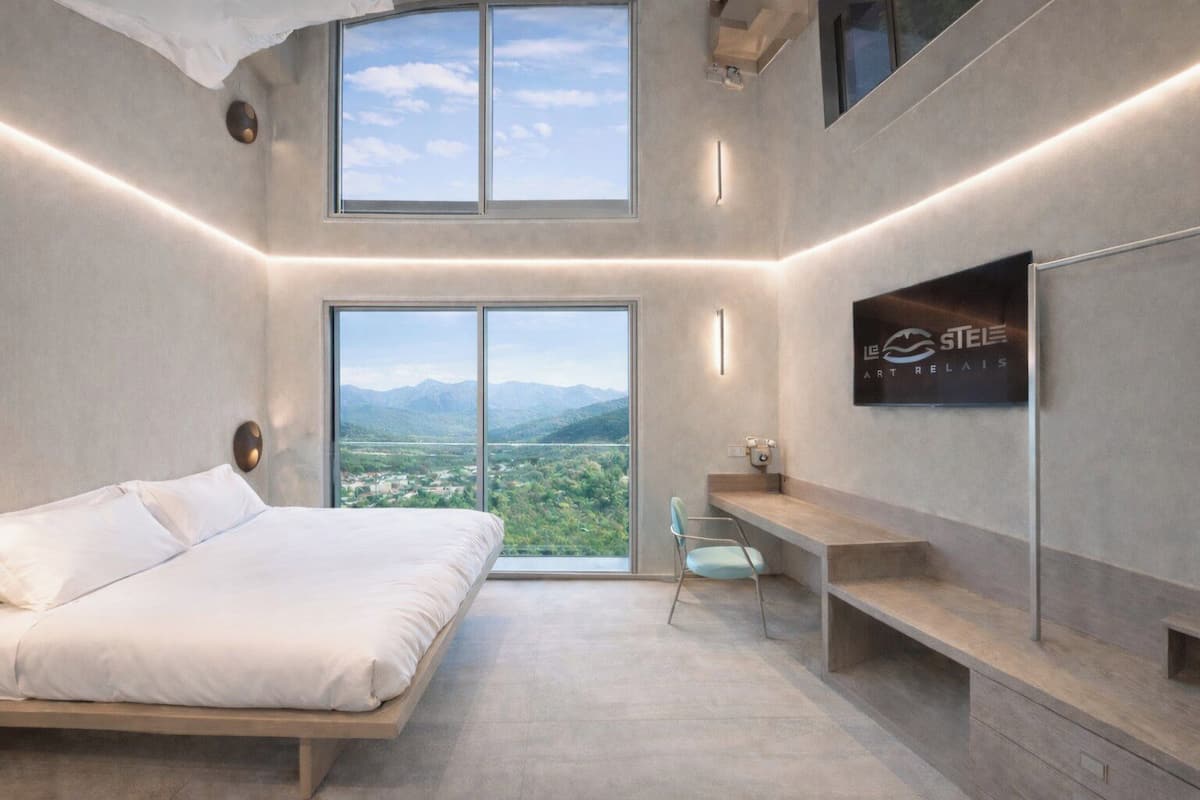 Un dormitorio moderno con una cama, un escritorio y un ventanal que ofrece vistas a la montaña.