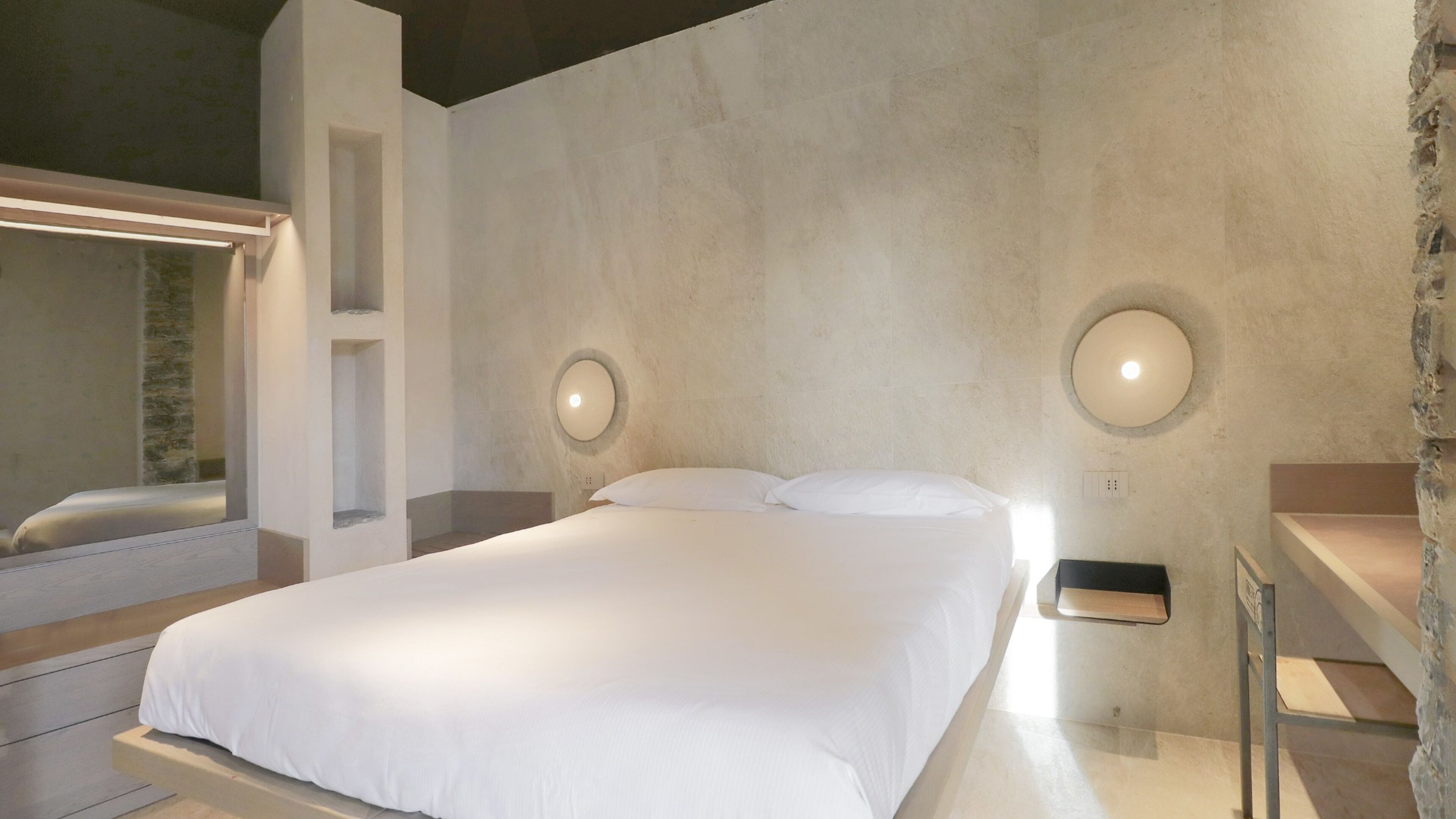 Een moderne slaapkamer met een groot bed, twee wandlampen, een inbouwbak en een accentmuur van steen.