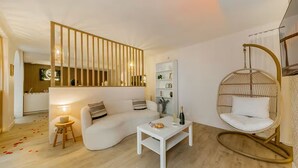 Una sala moderna con un sofá blanco, una mesita de centro blanca, una silla colgante y un separador de madera.