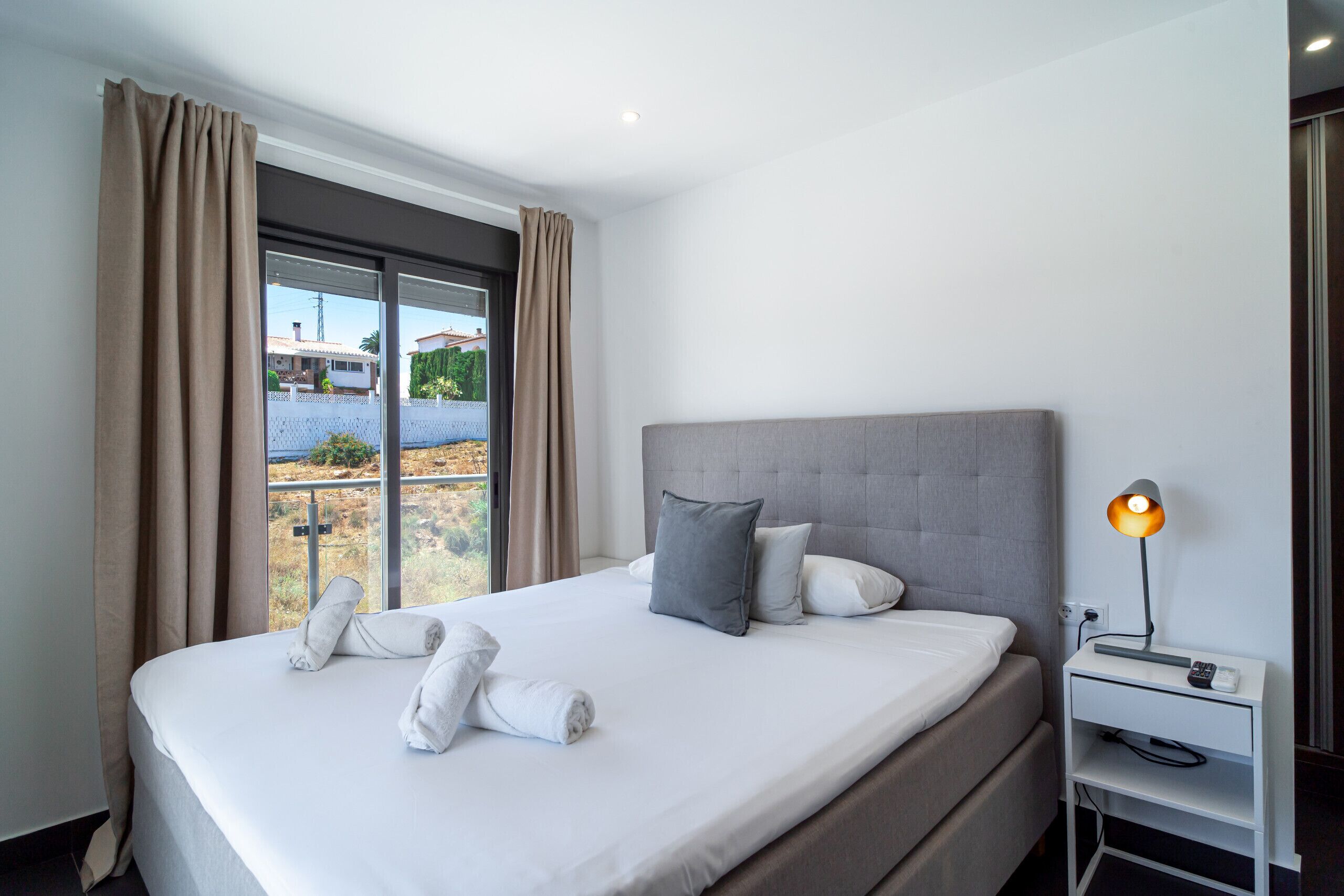 Une chambre d’hôtel avec un grand lit, une table de chevet avec une lampe et une vue sur un quartier résidentiel par la fenêtre.