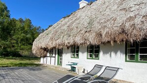 Ein Haus mit einem Strohdach, einer Holzterrasse, zwei Liegestühlen und einem kleinen Tisch.