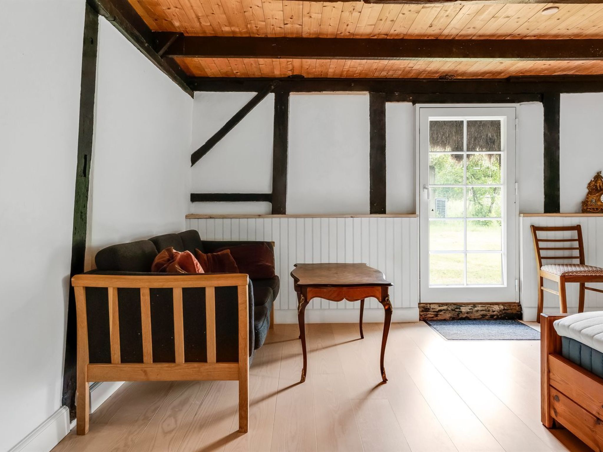 A room with a wooden ceiling, a window with a view of greenery, a wooden bench, and a table.