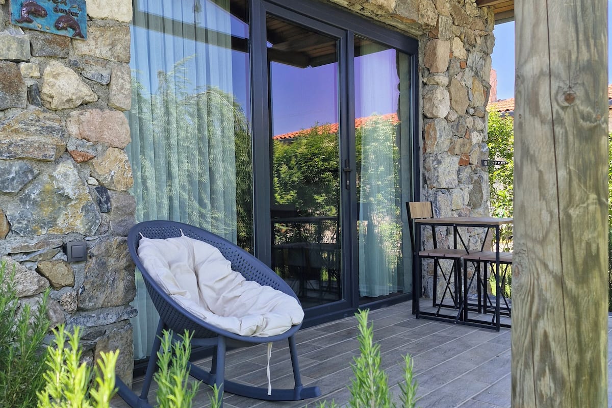 A stone building with a glass door, a wicker chair, and a table with chairs outside.