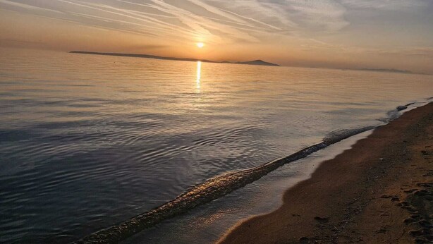 A beach with a calm sea, a visible shoreline, and a distant landmass. - Mavriya (Ezine)