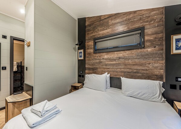 Ein modernes Hotelzimmer mit einem großen Bett, einer Wand mit Holzvertäfelung, einem kleinen Nachttisch und einem gerahmten Bild.