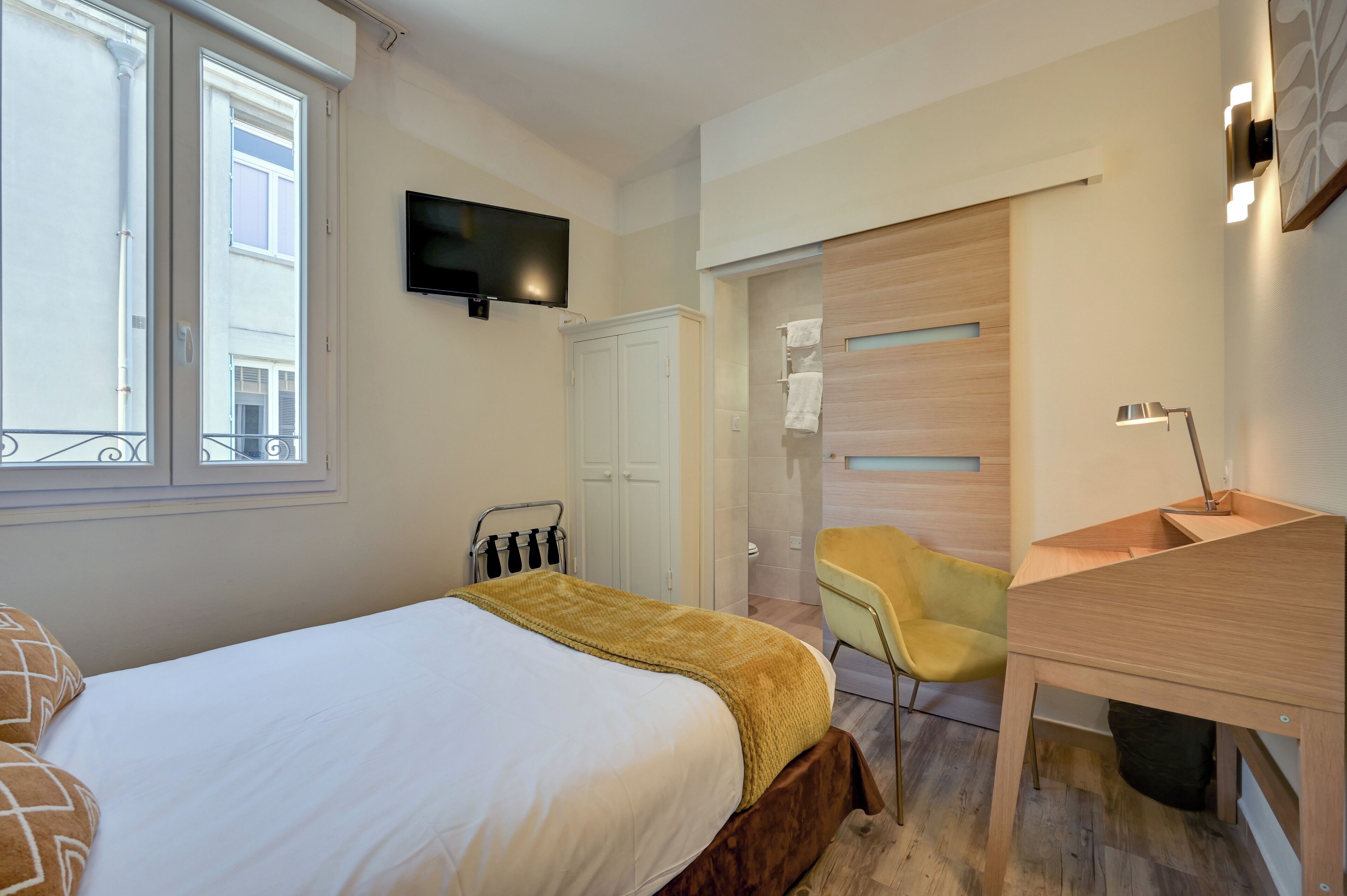 Ein modernes Hotelzimmer mit Bett, Schreibtisch, Sessel, Fernseher und einer Schiebetür zum Badezimmer.