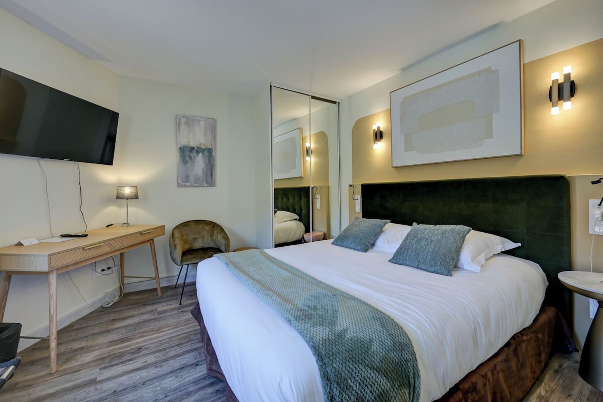 Une chambre d’hôtel avec un lit, un bureau, une chaise, une télévision et un miroir.