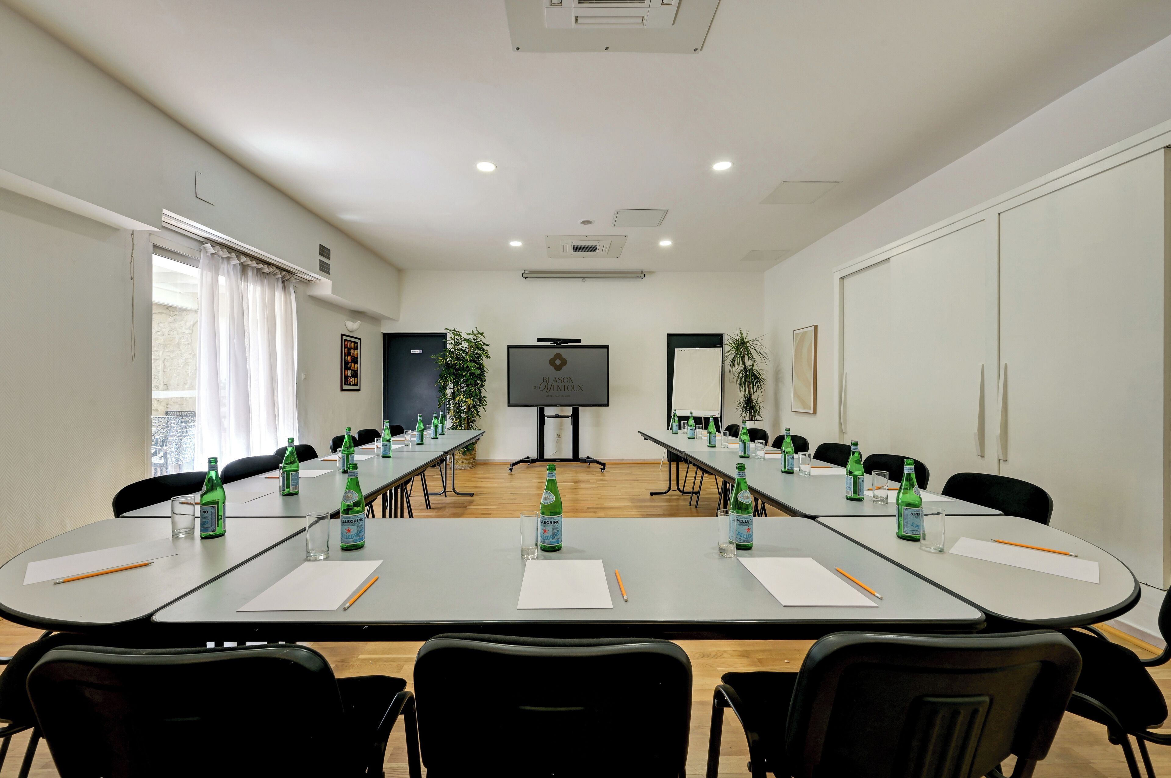 Un salón de conferencias con una larga mesa, sillas, una pantalla de proyector y una pizarra.
