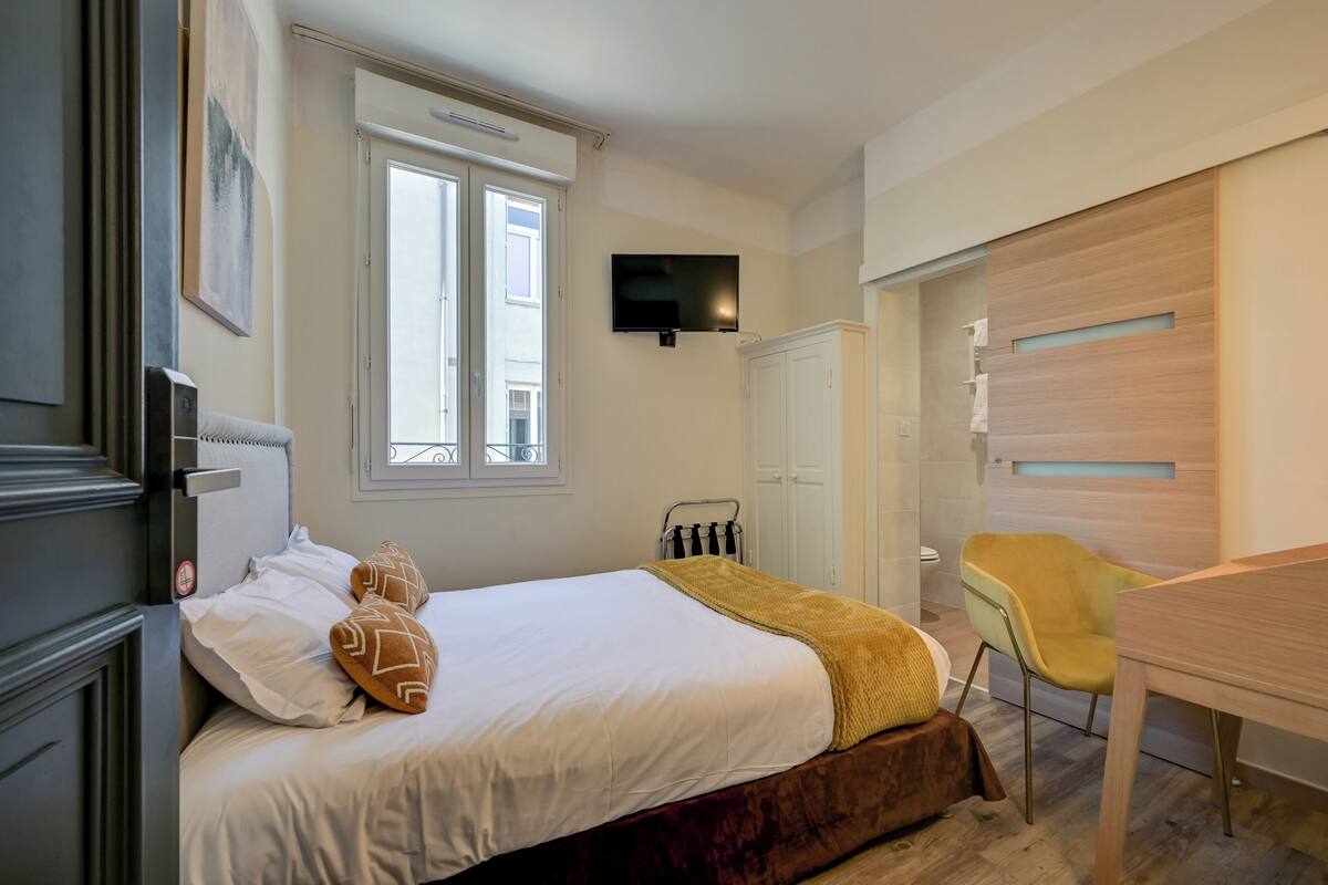 Une chambre à coucher avec un lit, un téléviseur fixé au mur, une fenêtre, un bureau et une chaise.