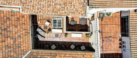 Vue aérienne d’une terrasse sur le toit, avec un espace repas, des sièges d’extérieur et un petit jardin.