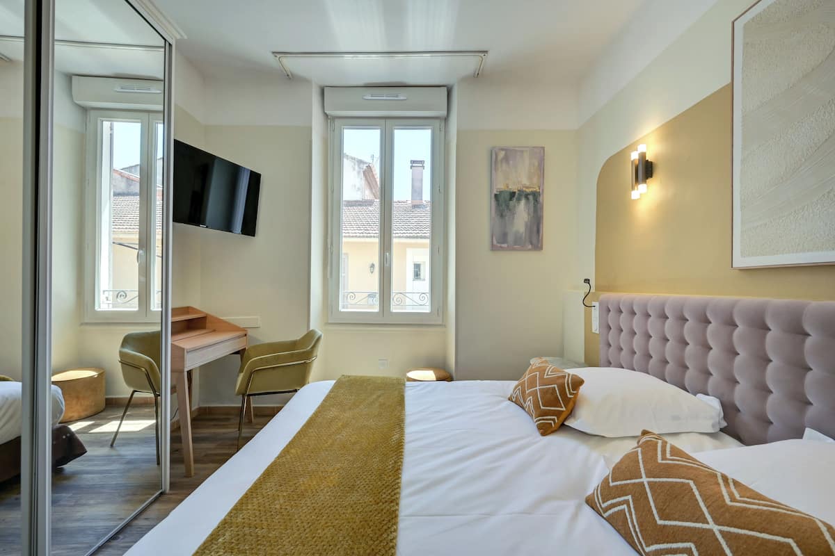 Une chambre d’hôtel moderne équipée d’un lit, d’un bureau et d’une chaise, d’un téléviseur à écran plat et d’une grande fenêtre.