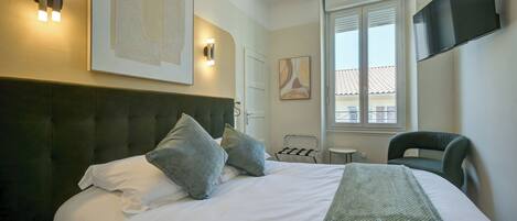 A hotel room with a large bed, a flat-screen TV mounted on the wall, and a window with a view of the outside.