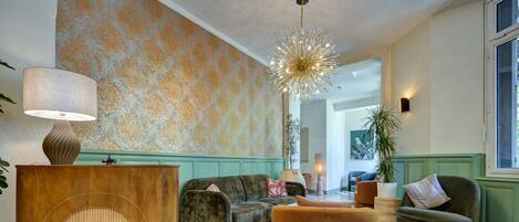 A living room with a patterned wallpaper, a modern chandelier, and a wooden sideboard.