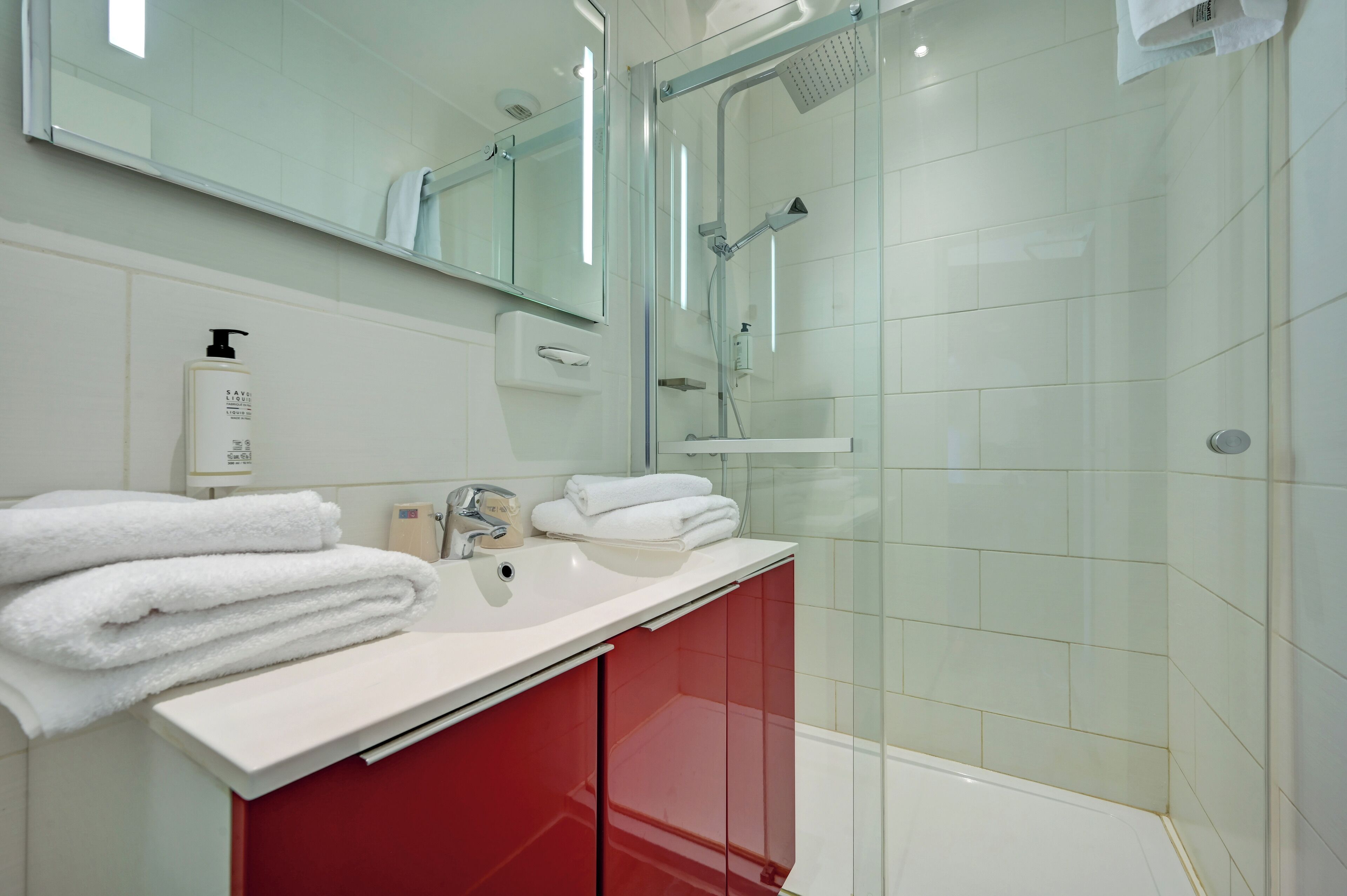 Une salle de bain moderne avec une douche à parois de verre, un lavabo blanc et des meubles rouges.