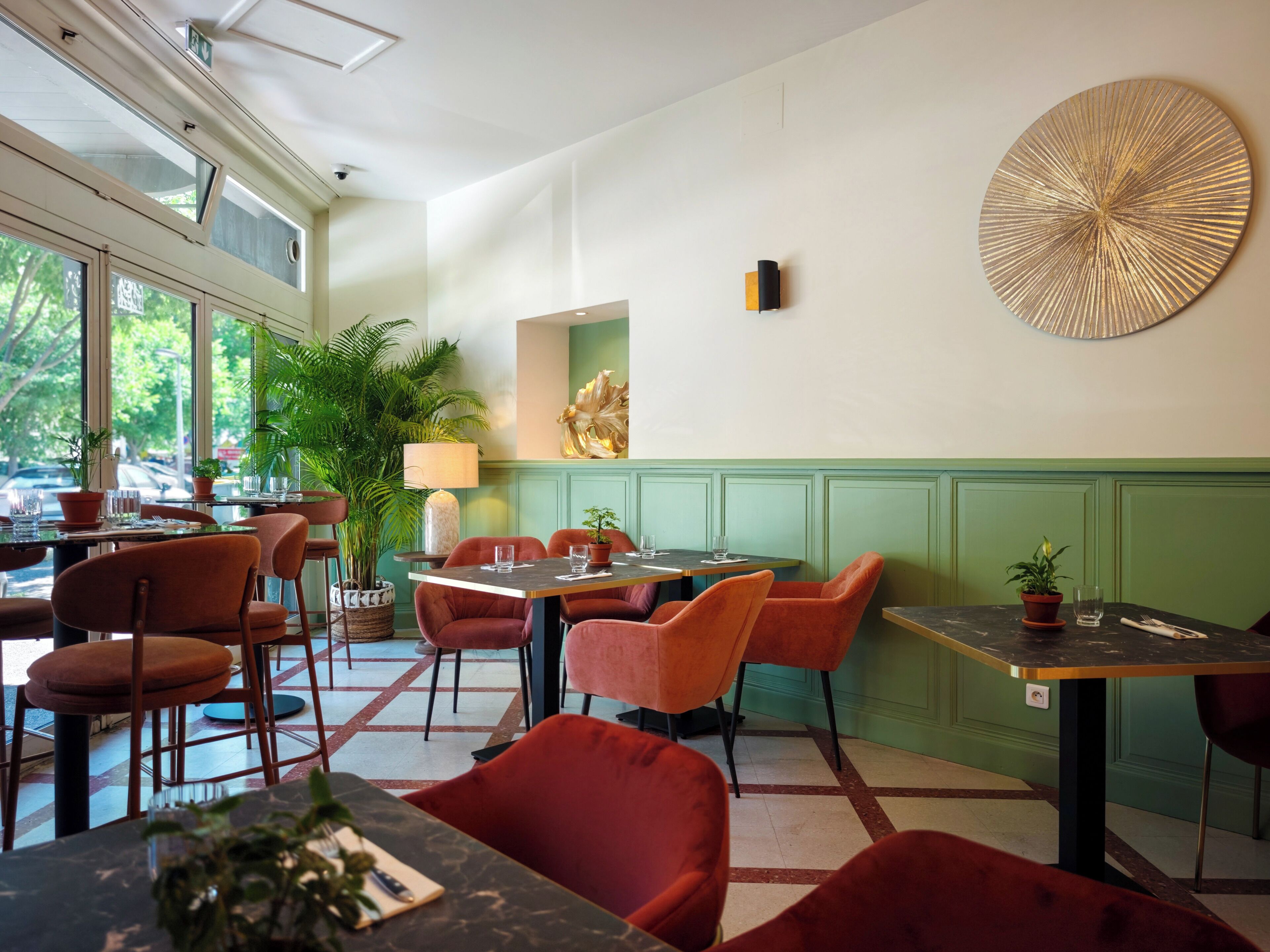 En restaurang med röda stolar och bord, krukväxter och en stor väggdekoration.