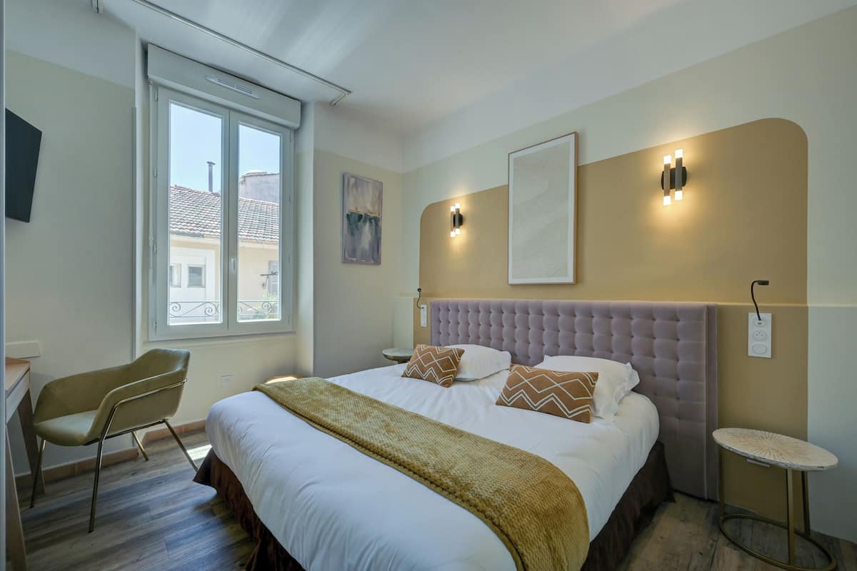 Une chambre avec un grand lit, une chaise, une table de chevet et une fenêtre.