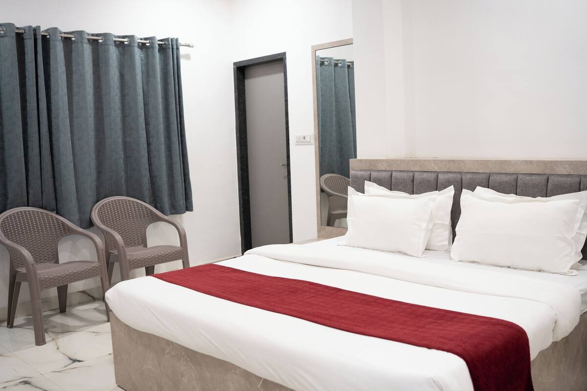 Ein Hotelzimmer mit einem Bett, zwei Korbstühlen, einer roten Tagesdecke und einem grauen Kopfteil.