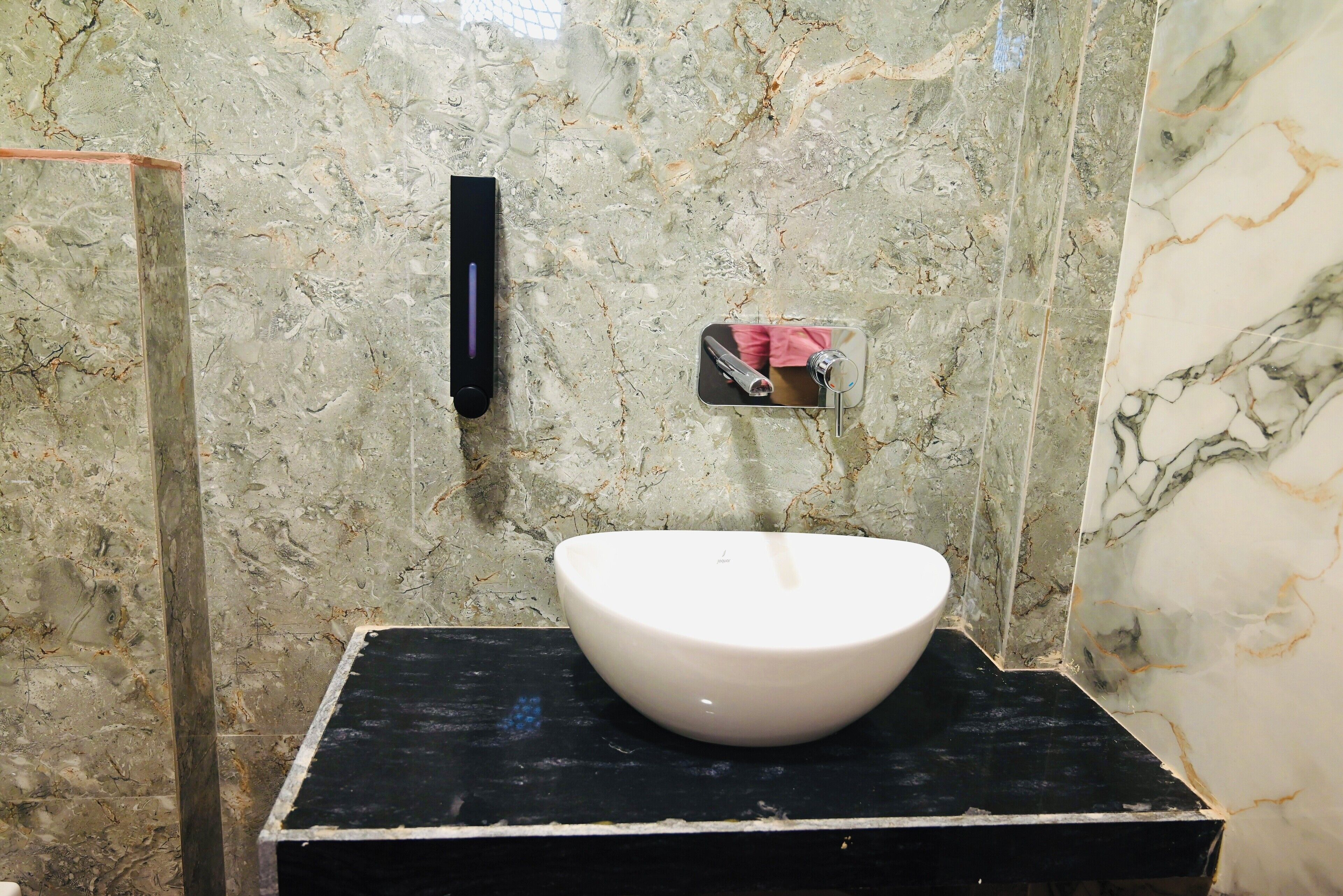 A bathroom with a white sink on a black countertop, a hand dryer, and a towel dispenser.