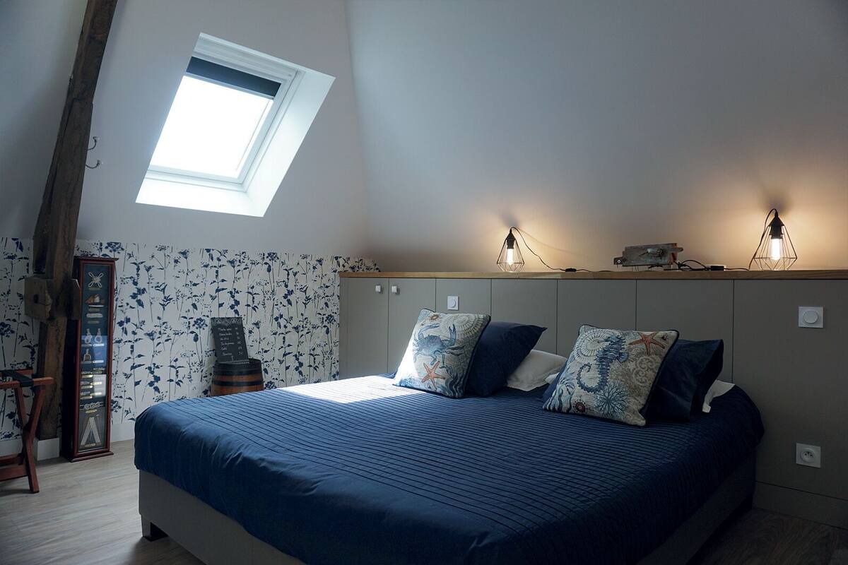 A bedroom with a large bed, a skylight, a wardrobe, and a shelf with decorative items.