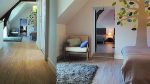Une chambre de style loft moderne, avec un plafond en pente, des poutres en bois, une grande fenêtre et une fresque représentant un arbre sur le mur.
