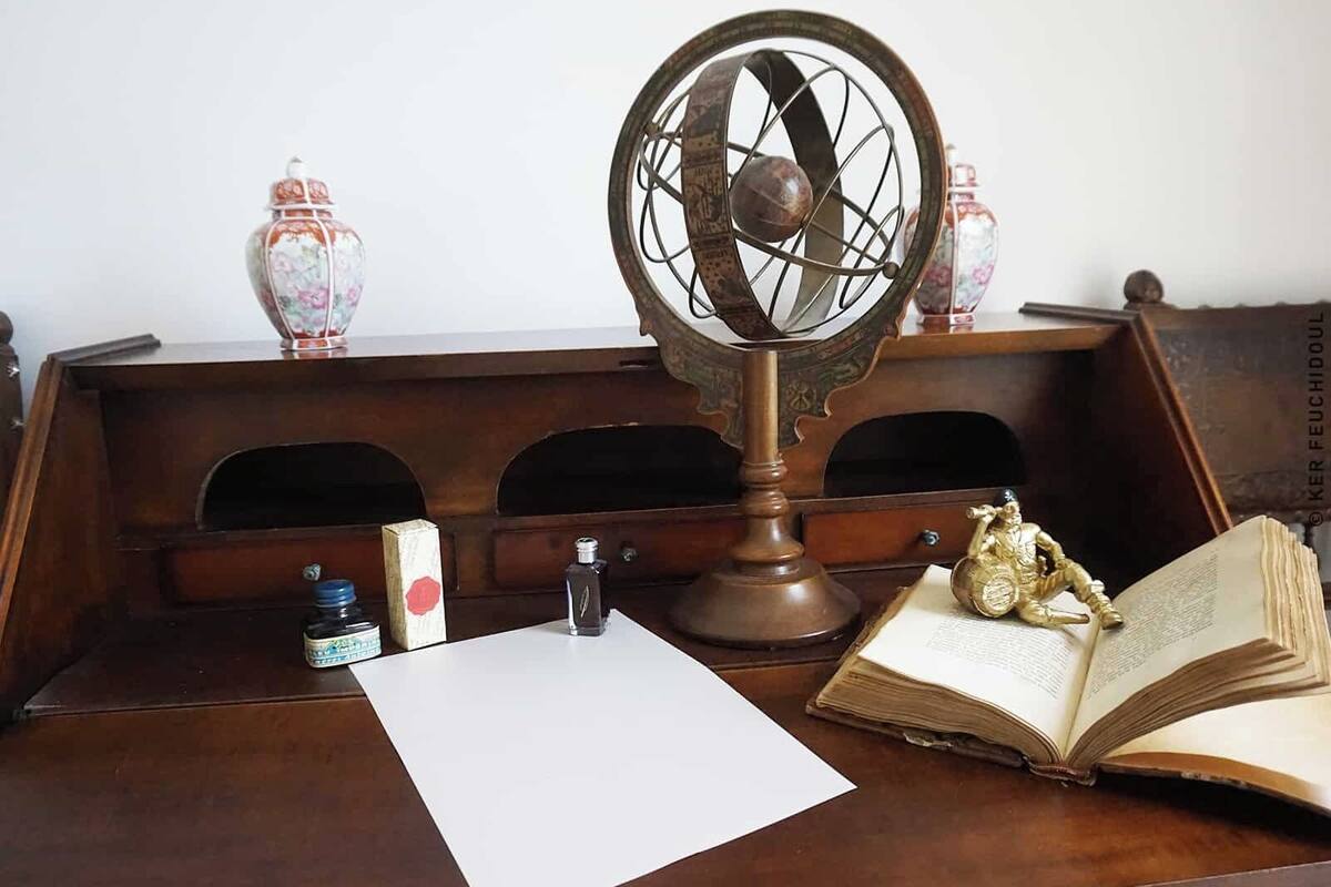A wooden desk with a vintage globe, an open book, a bottle, and a small figurine.