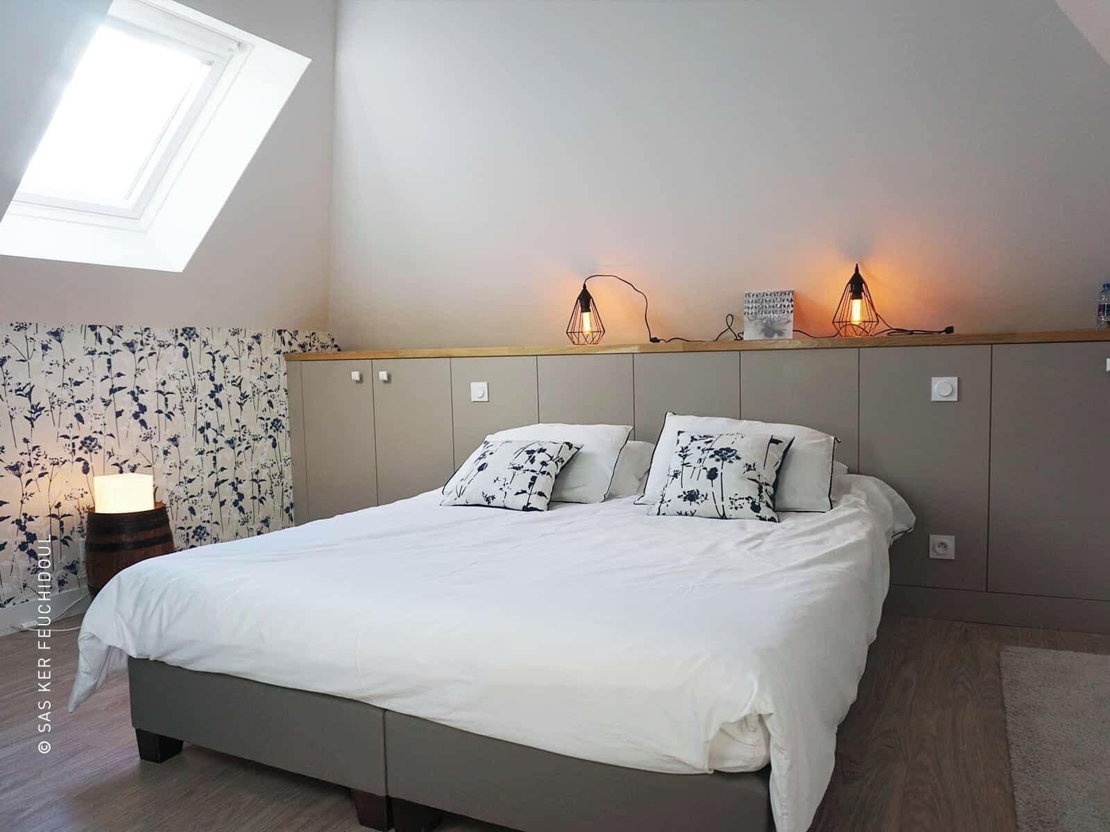 A bedroom with a bed, a nightstand, a lamp, and a skylight.