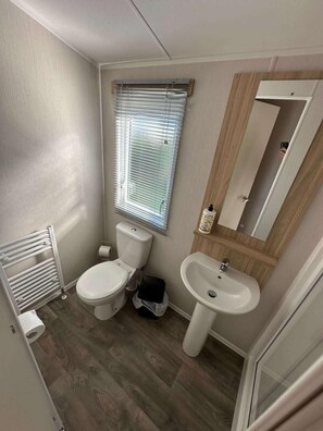 A compact bathroom with a toilet, sink, and window with blinds. - Trecco Bay - Sleeps 6 - Pet Friendly - Parking (Porthcawl)