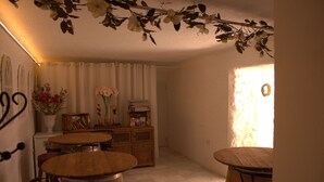 A cozy dining area with wooden tables and chairs, a white vase with flowers, and a bookshelf. - RUSTIC & ROMANTIC ROOM (Cuevas de Almanzora)