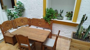 Une table à manger en bois, accompagnée de quatre chaises, entourée de plantes en pot et de cactus.