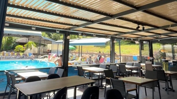 An outdoor dining area with tables and chairs, a pool in the background, and a covered roof structure. - Villapark (Bartin)