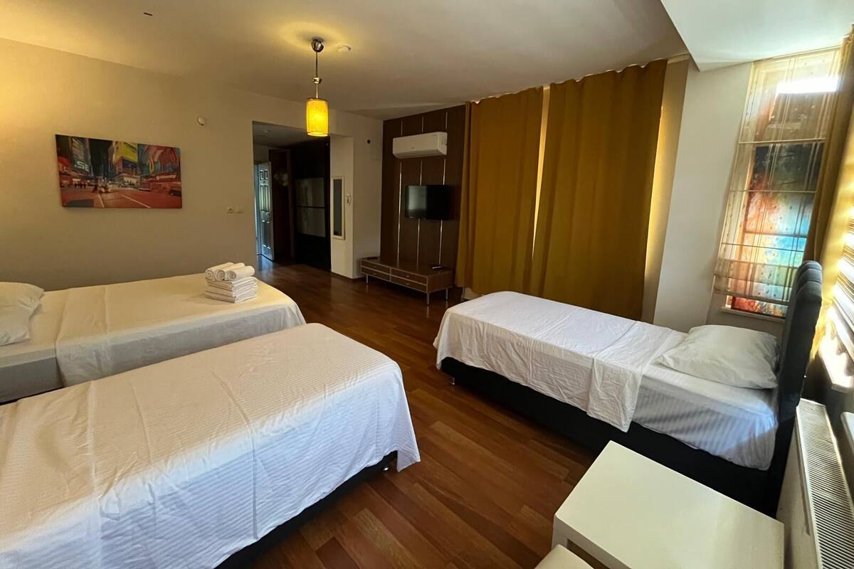 A hotel room with two single beds, a small table, a TV, and a painting on the wall.