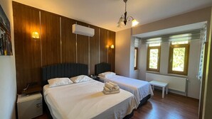 A hotel room with two beds, wooden paneling, an air conditioning unit, a chandelier, and windows with views. - Villapark (Bartin)