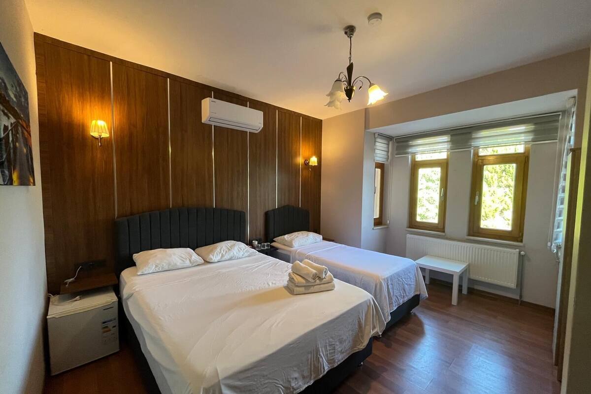 A hotel room with two beds, wooden paneling, an air conditioning unit, a chandelier, and windows with views.
