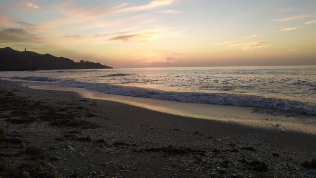 Una spiaggia con le onde, una costa lontana e un tramonto.