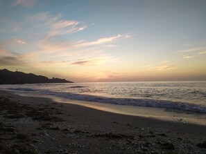 Una playa con olas, una costa lejana y un atardecer.
