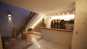 Angolo bar con parete in pietra, bancone in legno, sgabelli e una scala.