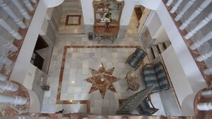 Eine beeindruckende Lobby mit Marmorböden, einem zentralen sternförmigen Design, einem großen Spiegel und einer Sitzecke mit blau-weiß gestreiften Sofas.