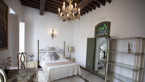 A bedroom with a bed, a chandelier, a mirror, and a wooden chair.