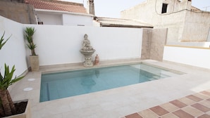 A swimming pool with a statue and a small fountain, surrounded by a white wall and potted plants.